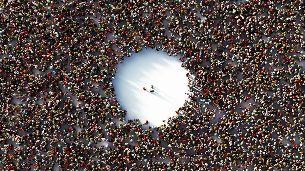 A packed crowd with a giant empty circle in the middle is shown from above. Three people stand in the empty space..